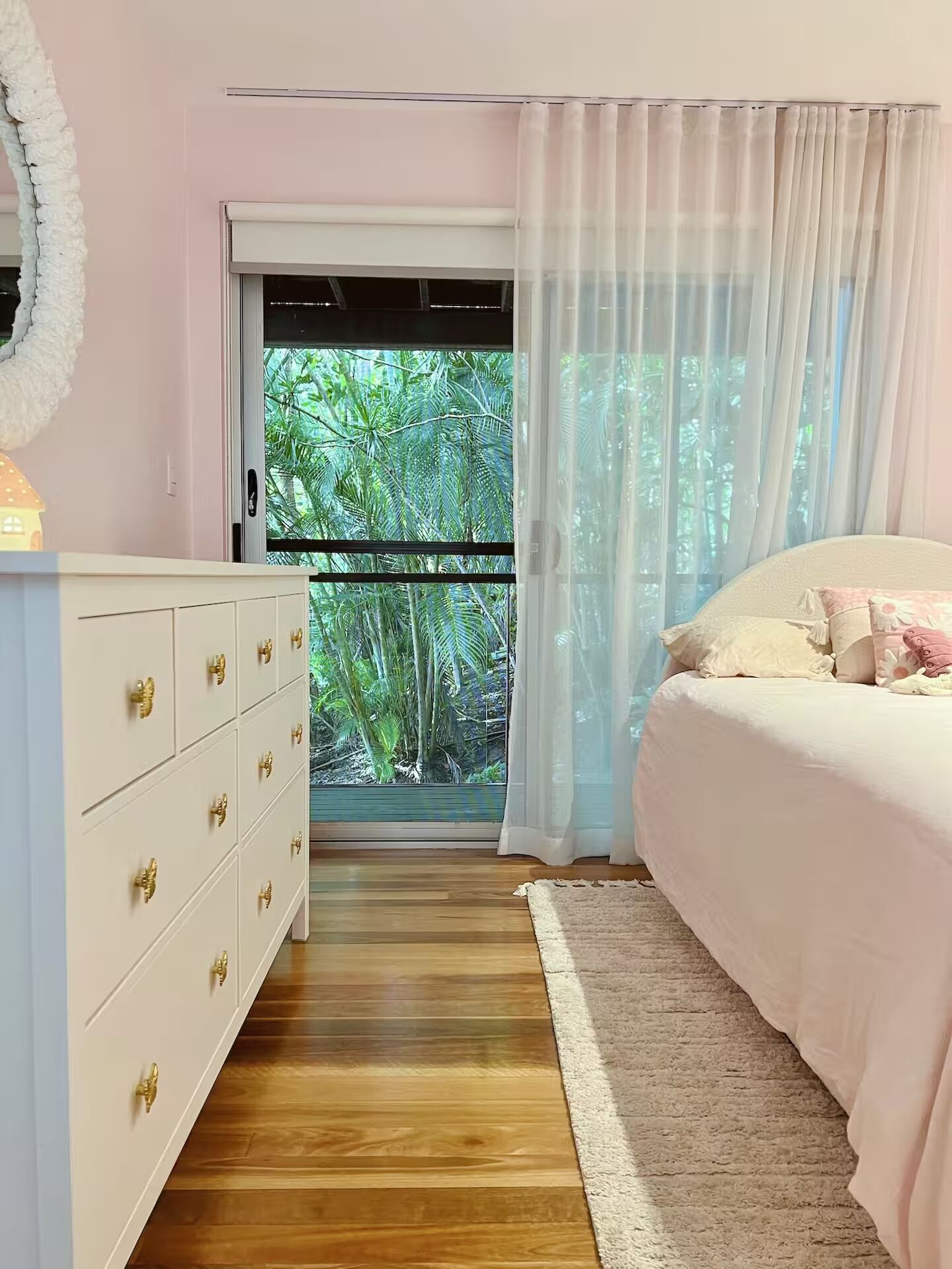 A bedroom with a bed, a dresser, a window with curtains, and a view of greenery outside.