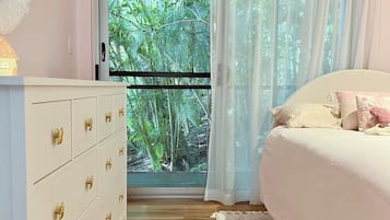 A bedroom with a bed, a dresser, a window with curtains, and a view of greenery outside.