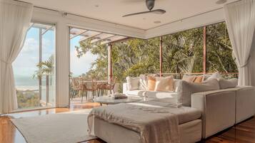 A modern living room with a large sofa, a coffee table, and a view of the ocean.