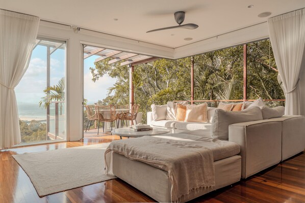 A modern living room with a large sofa, a coffee table, and a view of the ocean.