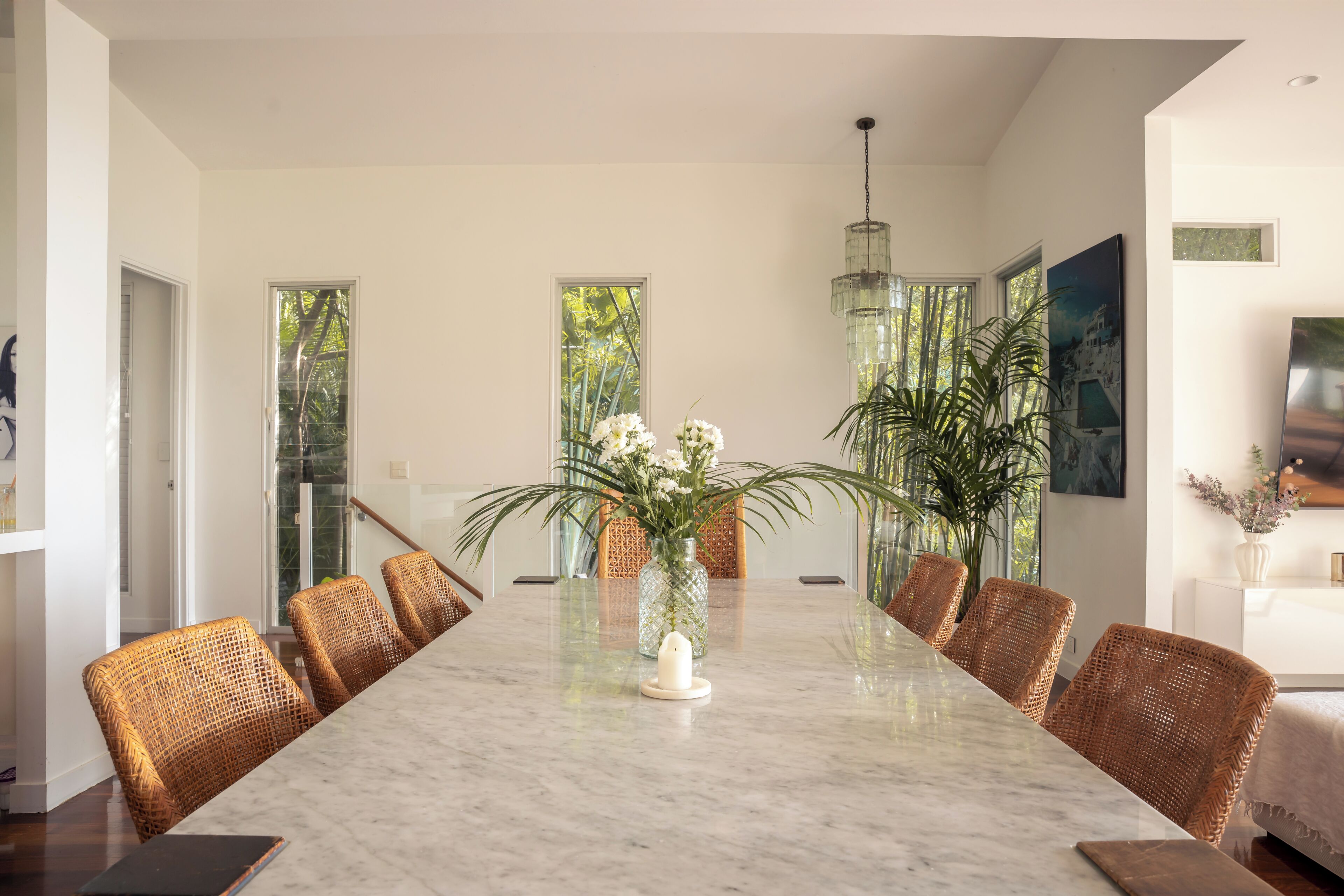 Un vaste espace dédié à la salle à manger, avec une table en marbre, des chaises en osier et de grandes fenêtres laissant entrer la lumière naturelle.