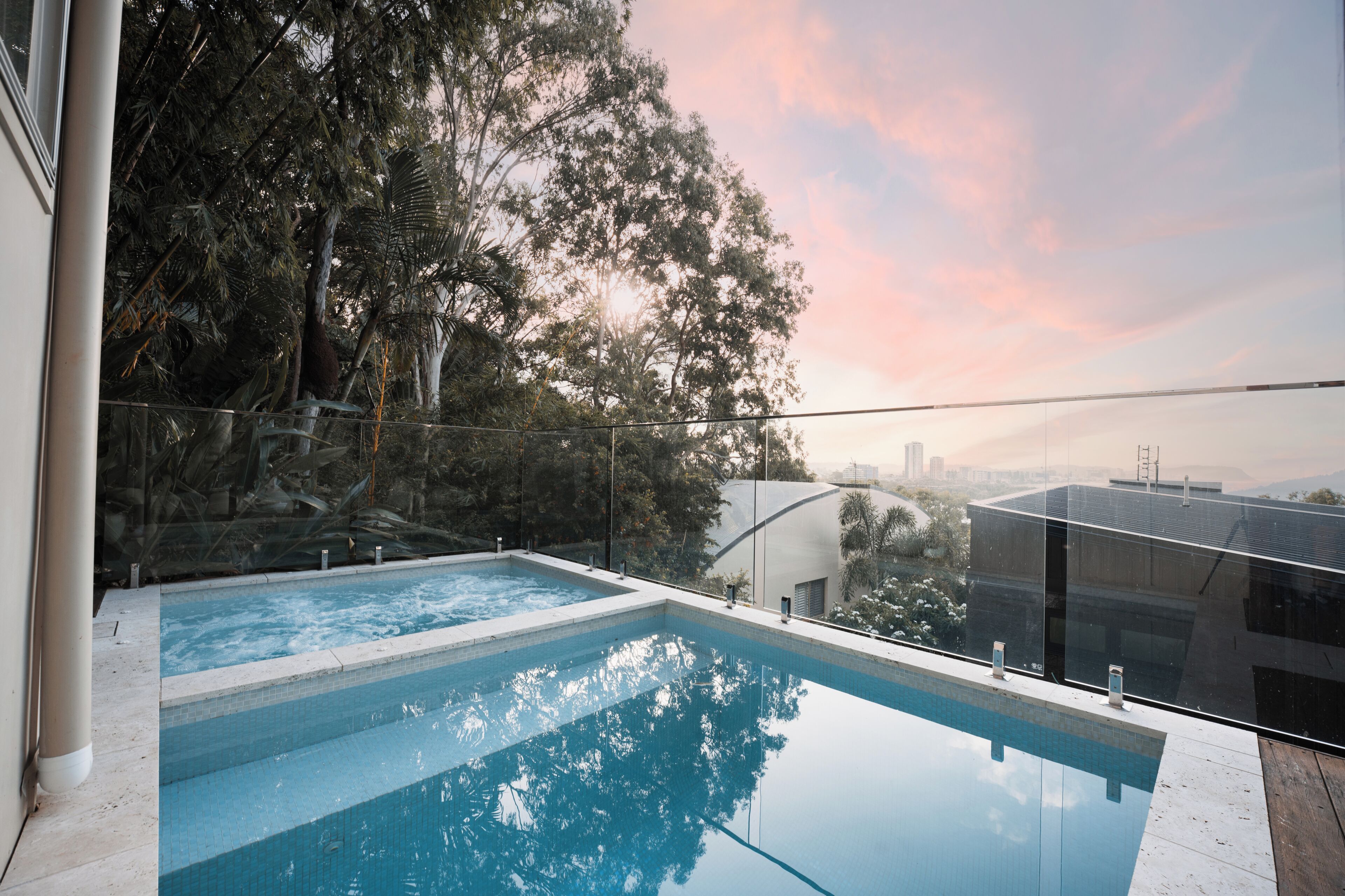 A swimming pool with clear water, surrounded by a glass barrier and trees.