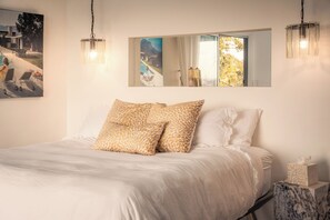 Une chambre à coucher avec un lit, des oreillers, une table de chevet, un miroir et un tableau accroché au mur.