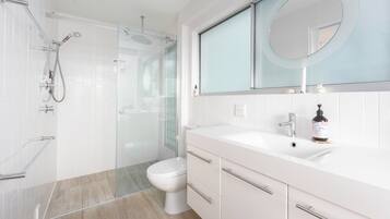 A modern bathroom with a glass shower enclosure, a toilet, a sink with a mirror, and a bottle of shampoo on the counter.