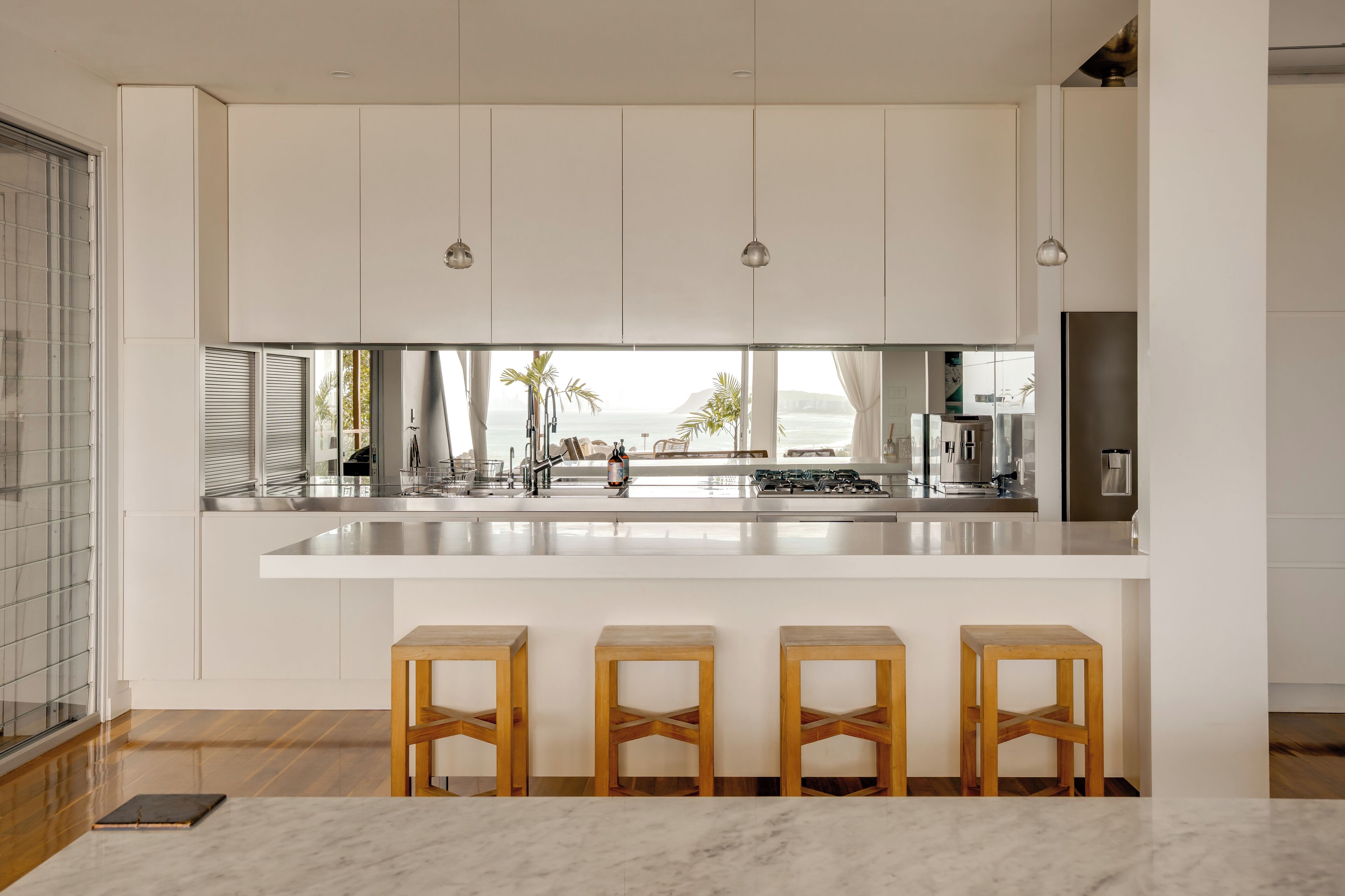A modern kitchen with white cabinetry, a large island with stools, and a view of the ocean.