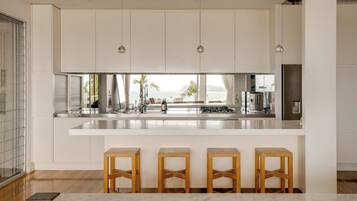 A modern kitchen with white cabinetry, a large island with stools, and a view of the ocean.