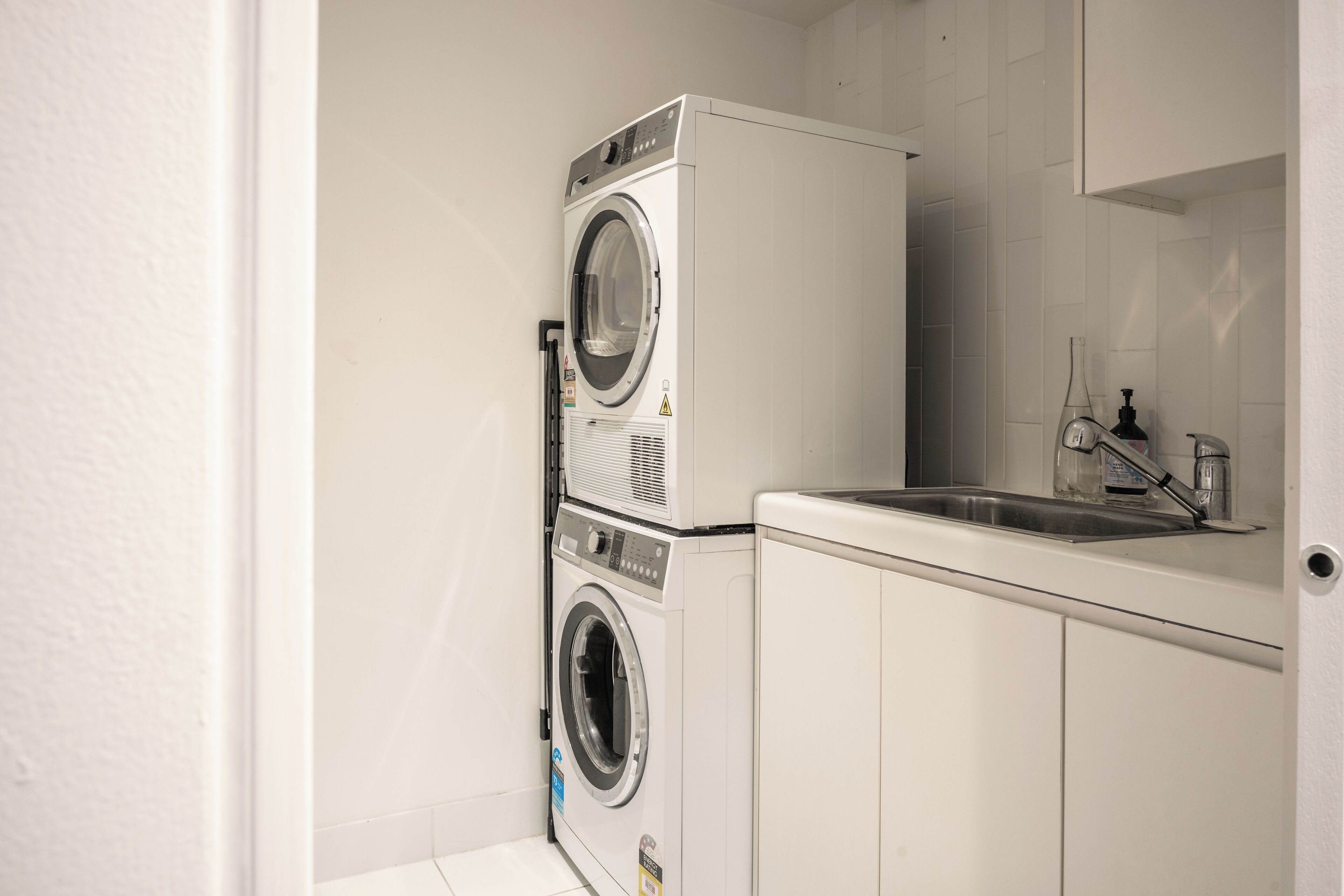 A laundry room with a stacked washer and dryer, a sink, and a mirror.