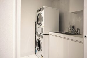 A laundry room with a stacked washer and dryer, a sink, and a mirror.