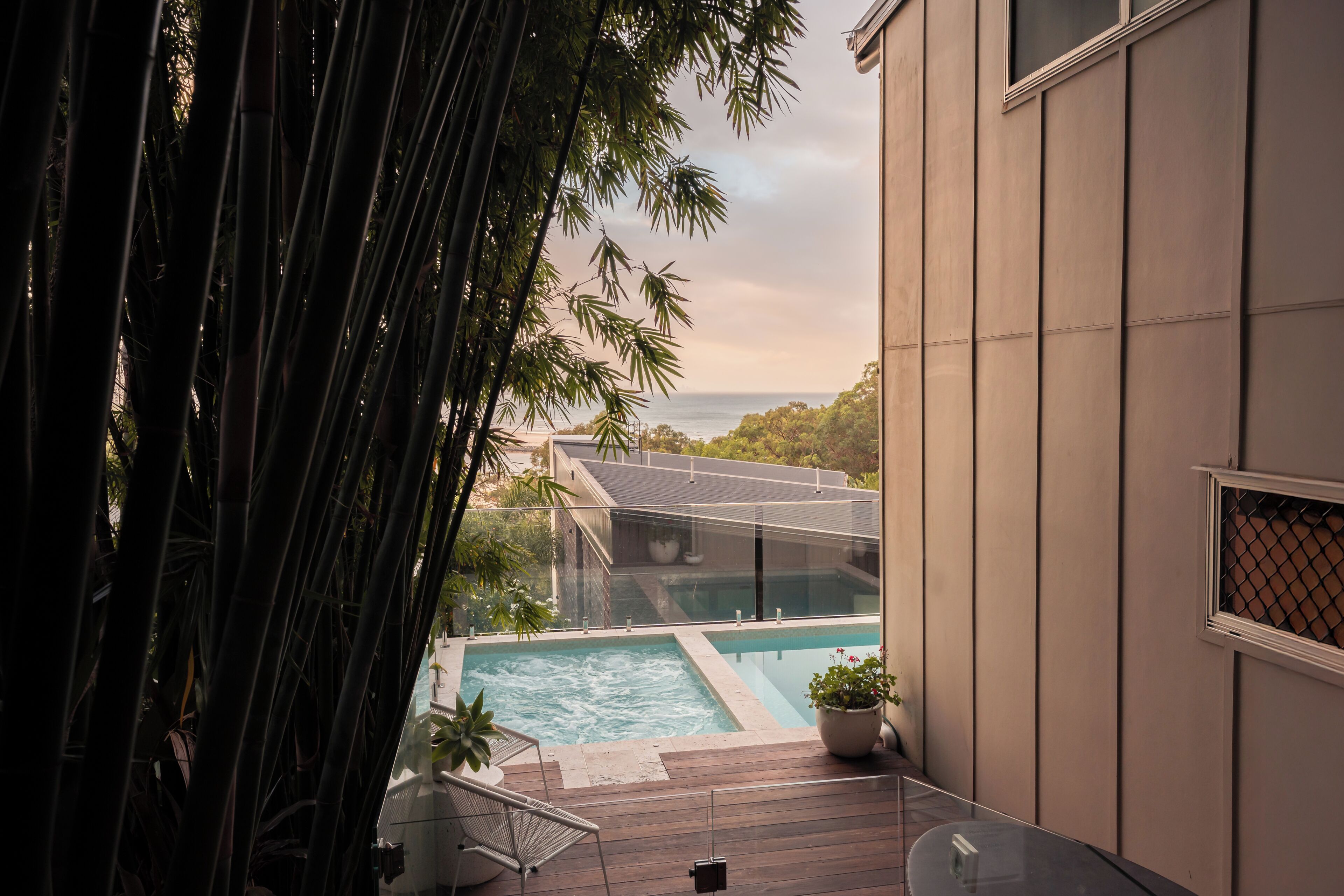 A modern pool area with clear glass boundaries, a wooden deck, and a view of the sea.