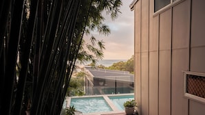 A modern pool area with clear glass boundaries, a wooden deck, and a view of the sea.