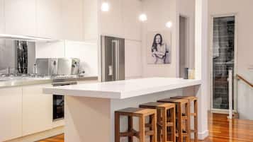 A modern kitchen with a central island, bar stools, stainless steel appliances, and a large window.