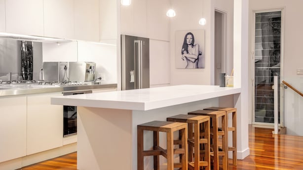 A modern kitchen with a central island, bar stools, stainless steel appliances, and a large window.