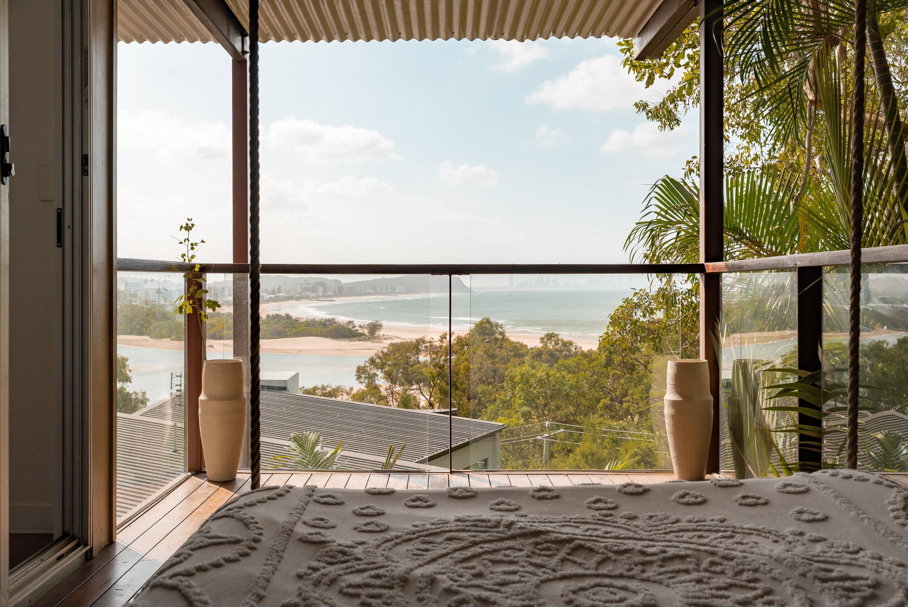 A room with large windows overlooking a beach and ocean, with a patterned rug on the floor.