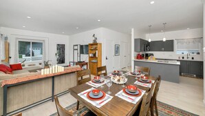 Una cocina moderna con armarios oscuros, una isla central y una zona de comedor con una mesa de madera dispuesta para seis comensales.