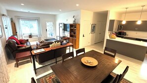 Una sala de estar moderna con sofá, mesa de centro y mesa de comedor. Hay una zona de cocina con microondas y fregadero.