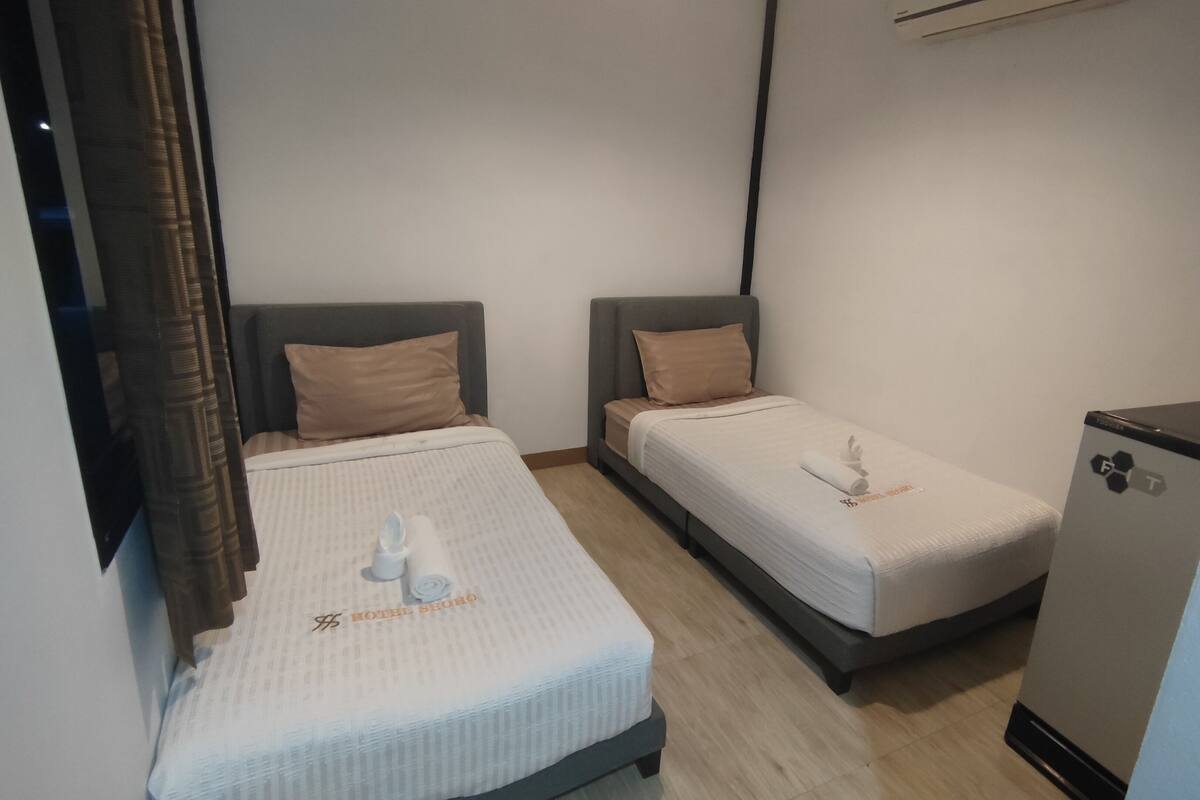 A hotel room with two single beds, a small desk, and a minibar.