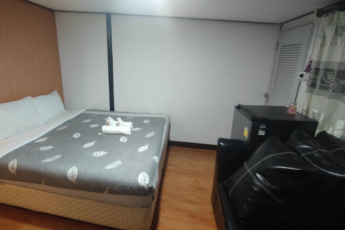 A neatly made bed with a leaf-patterned bedspread, a wooden headboard, and a black leather chair.