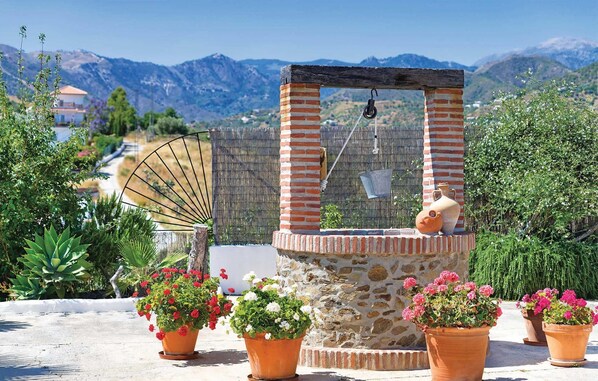 A rustic outdoor water fountain with a wooden structure, surrounded by potted plants and a scenic mountain backdrop. - Frigiliana villa: 2BR villa, private pool, A/C & dazzling views (Frigiliana)