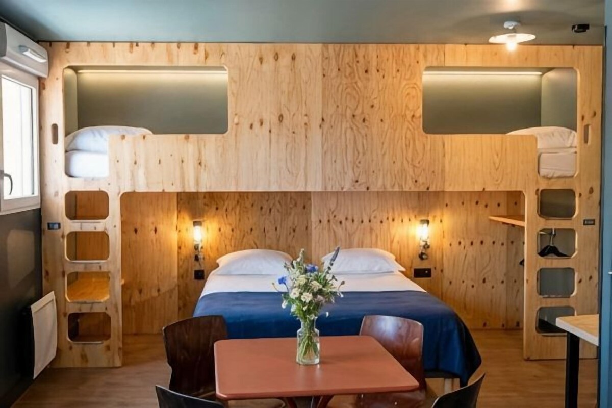 A bunk bed room with a table and chairs, a vase with flowers, and a wooden wall design.