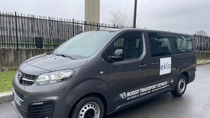A gray van with "ROISSY TRANSPORT EXPRESS" and "eklo" branding parked on a wet road. - Eklo Hotels Paris Roissy CDG Airport (Roissy-en-France)