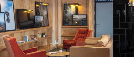 A cozy lounge area with wooden paneling, a large flat-screen TV, comfortable seating, and framed artwork on the walls.