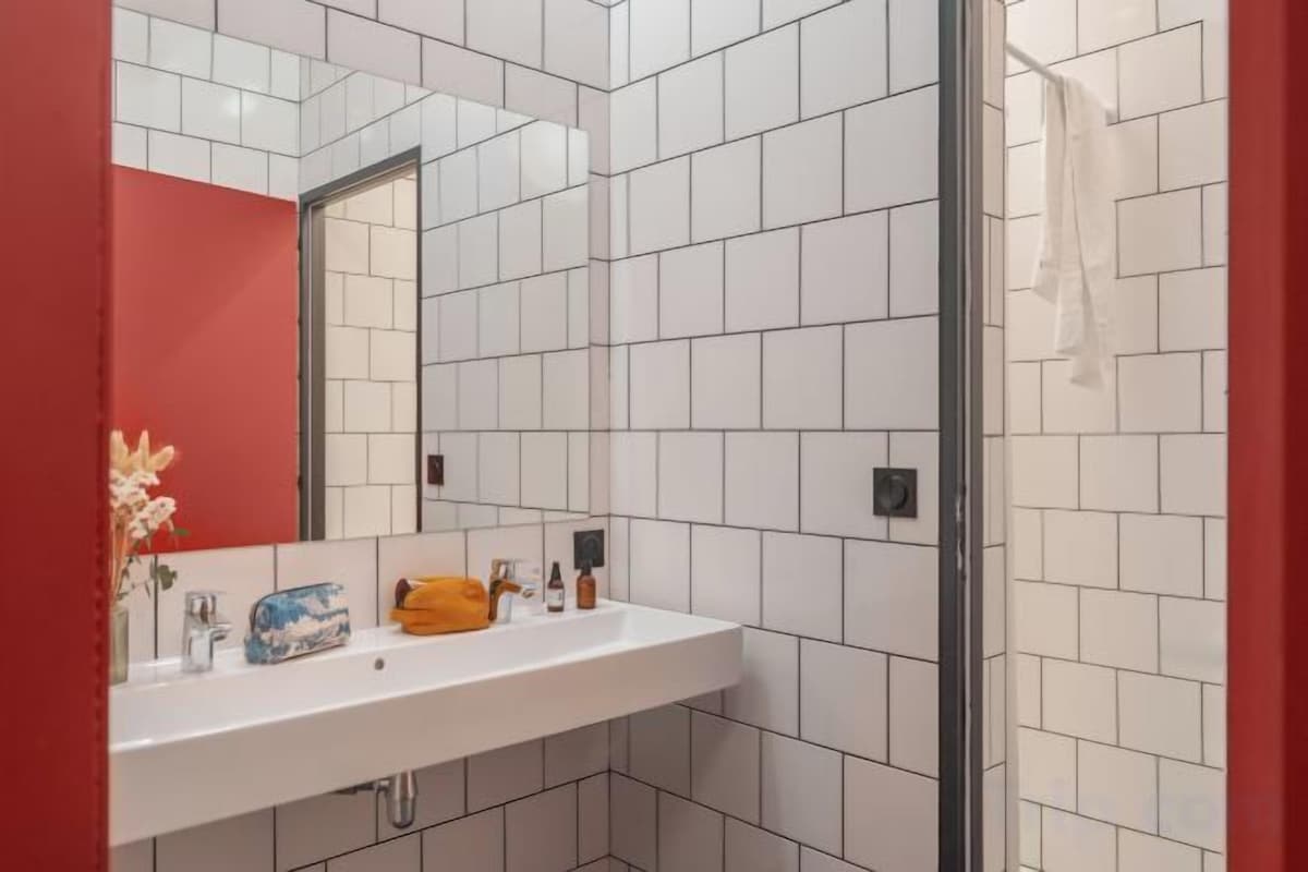 Ein Badezimmer mit weiß geflieste Wand, einer roten Akzentwand, einem weißen Waschbecken und einem Spiegel.