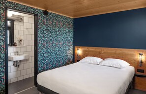 Camera da letto con testiera in legno, un letto bianco e un comodino con luce a parete.