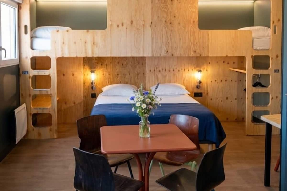 A room with a bunk bed, a table with chairs, and a vase with flowers.