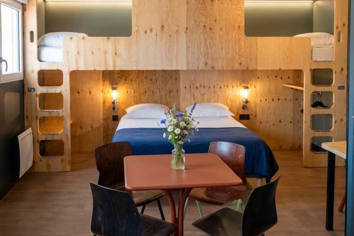 Een kamer met een stapelbed, een tafel met stoelen, en een vaas met bloemen.