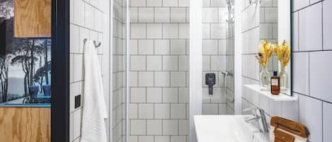A modern bathroom with white tiled walls, a wooden ceiling, a white sink, a mirror, and a shower enclosure.