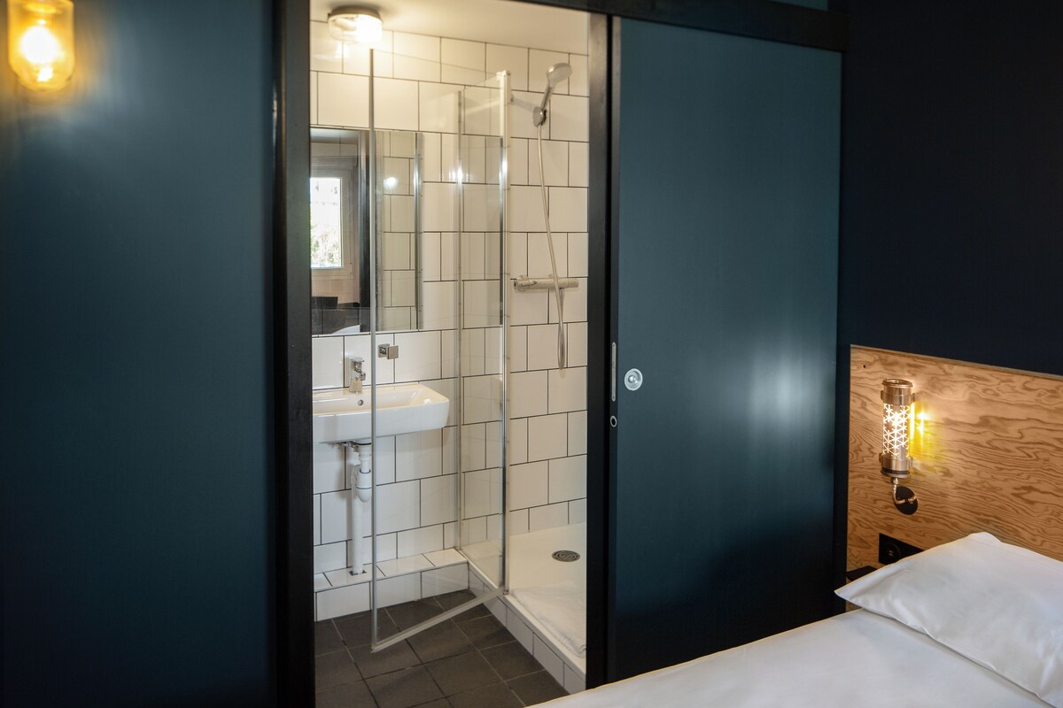 A modern bathroom with a glass shower enclosure, a white sink, and a wooden headboard with a wall-mounted light fixture.