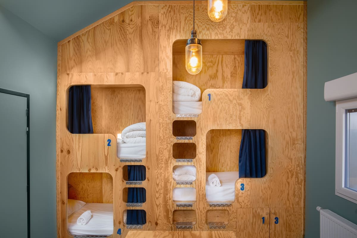 A wooden bunk bed room with numbered compartments, each containing a rolled-up towel.