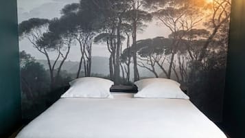 A bed with a white mattress, a headboard, and a pull-out section, set against a wall with a forest landscape mural.