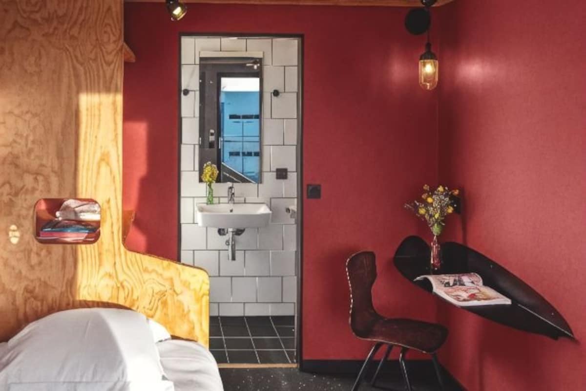 A modern room with a bed, a small sink, a mirror, a chair, and a magazine on a table.