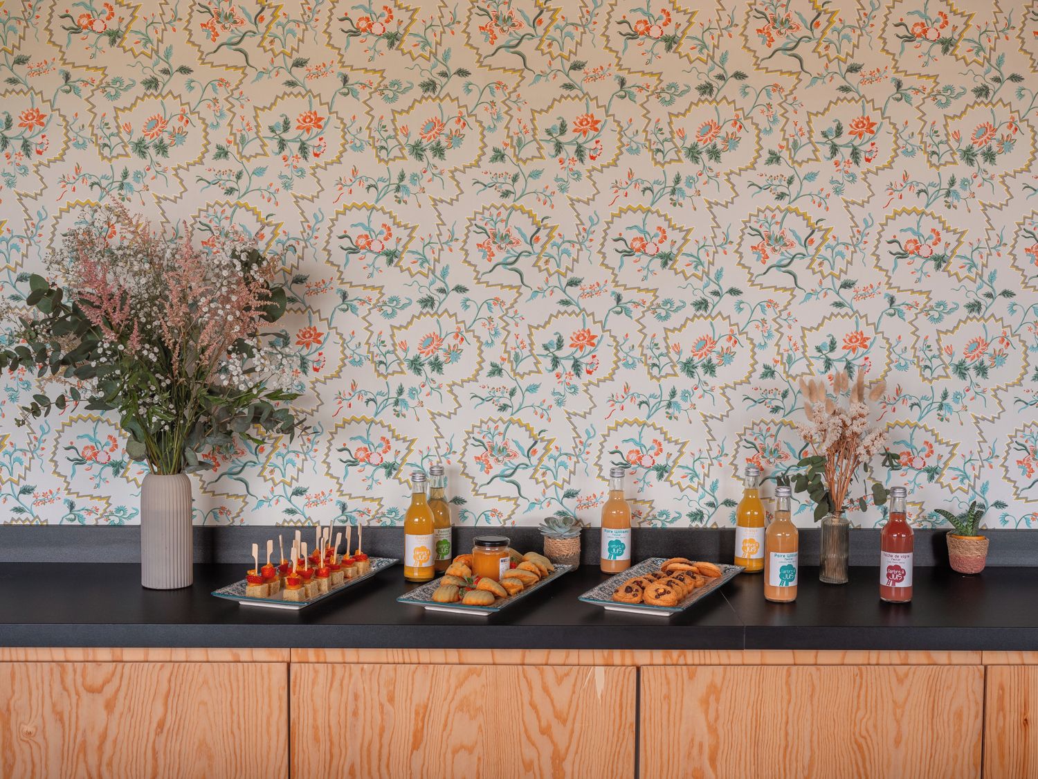 Una encimera de cocina con papel tapiz floral, varios alimentos y botellas.