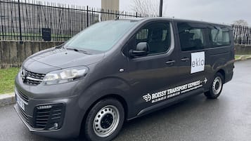 Una furgoneta gris con la marca 'ROISSY TRANSPORT EXPRESS' y 'eklo' estacionada en una calle mojada.