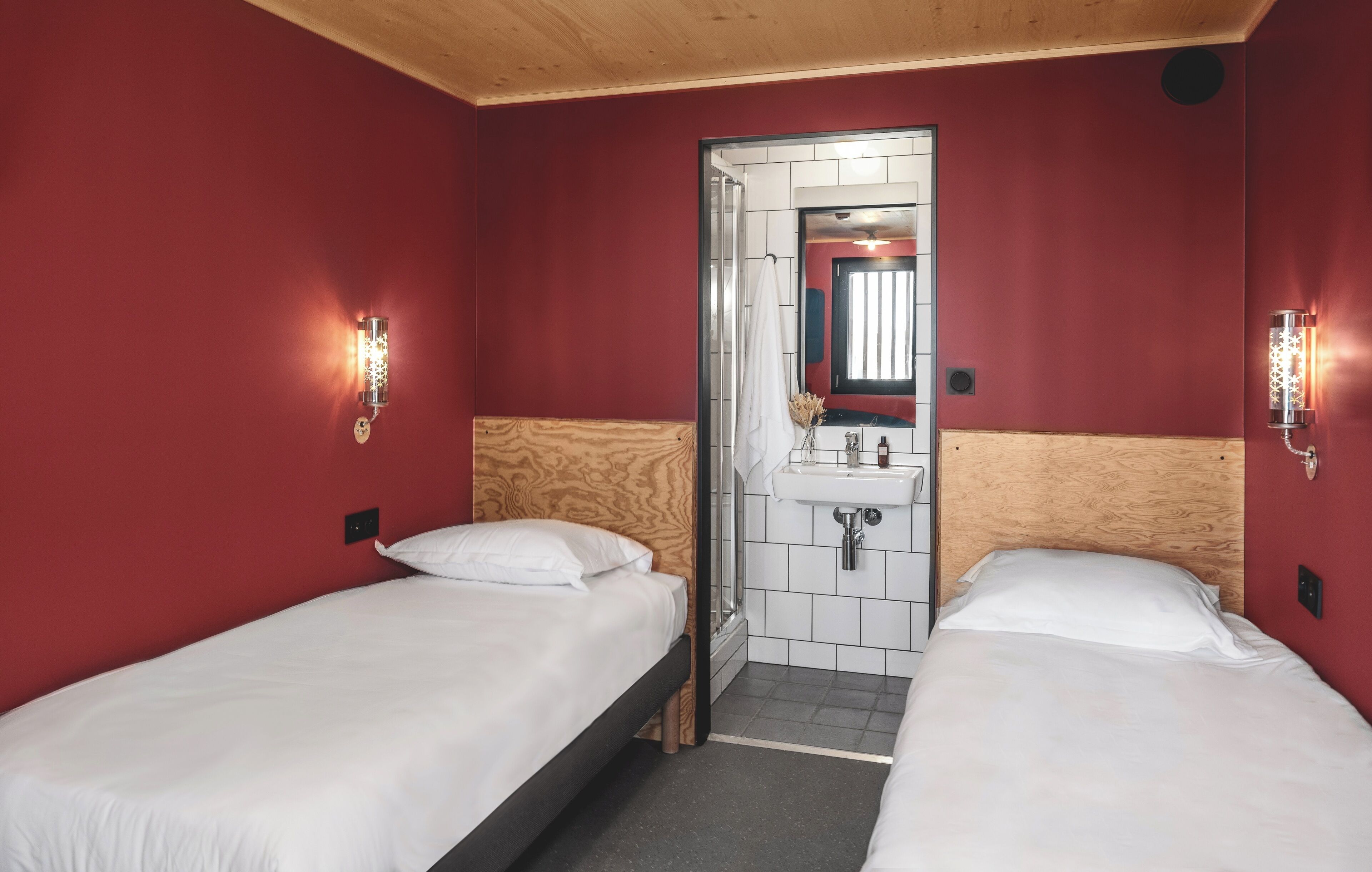 Une chambre avec deux lits, une tête de lit en bois, un petit lavabo et un miroir.