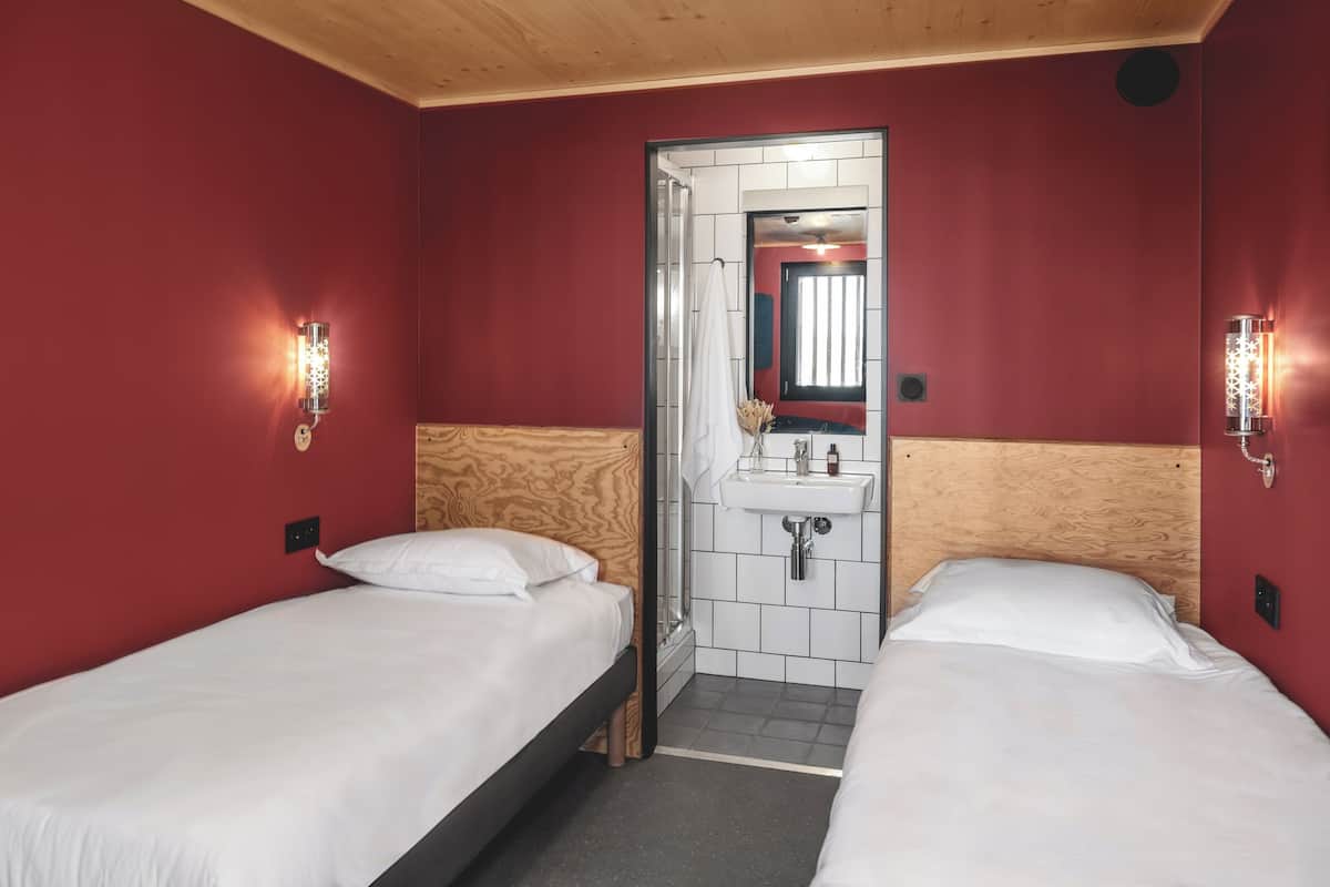 A small, compact room with two single beds, a wooden headboard, a small sink, and a mirror above it.