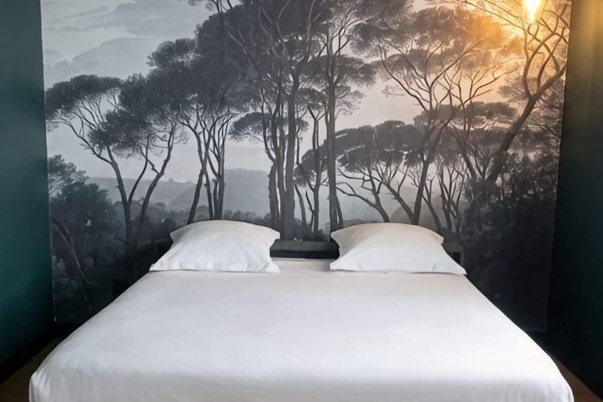 A bed with white linens in a room with a mural of trees and mountains on the wall.