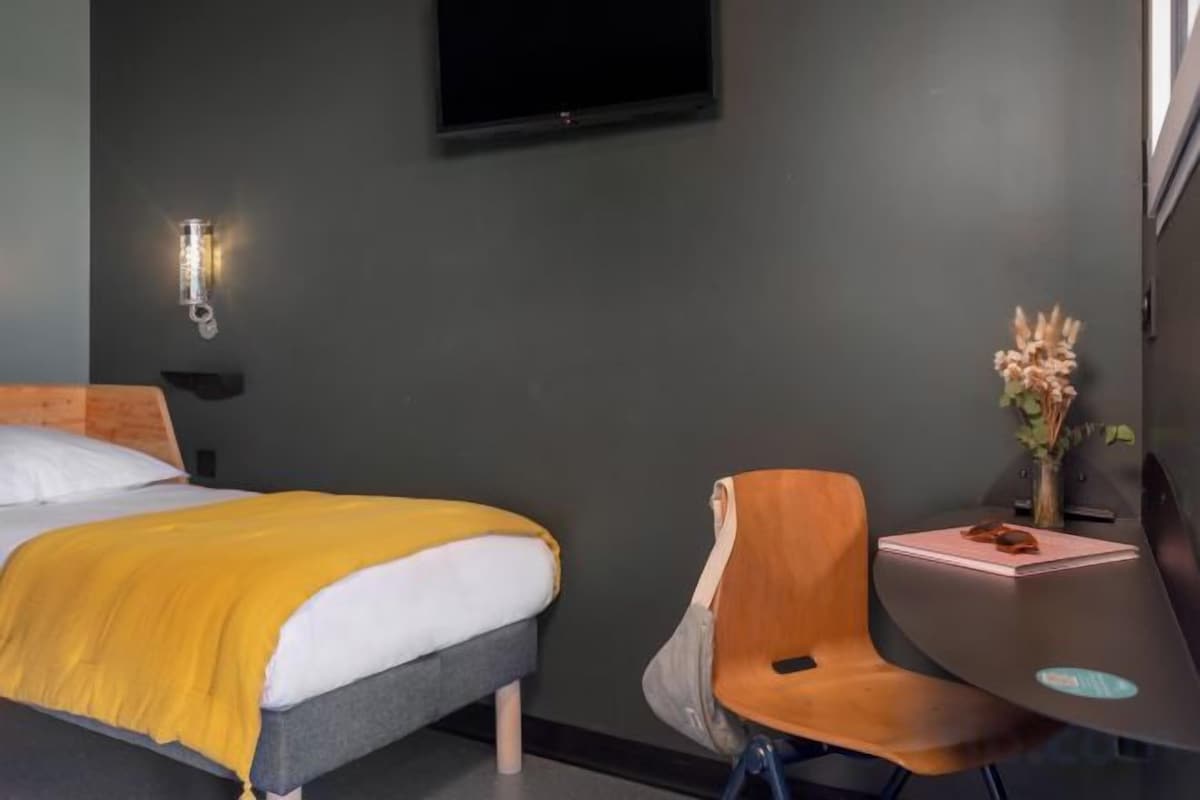 Ein Hotelzimmer mit einem Bett, einem Schreibtisch, einem Stuhl und einem an der Wand befestigten Fernseher.