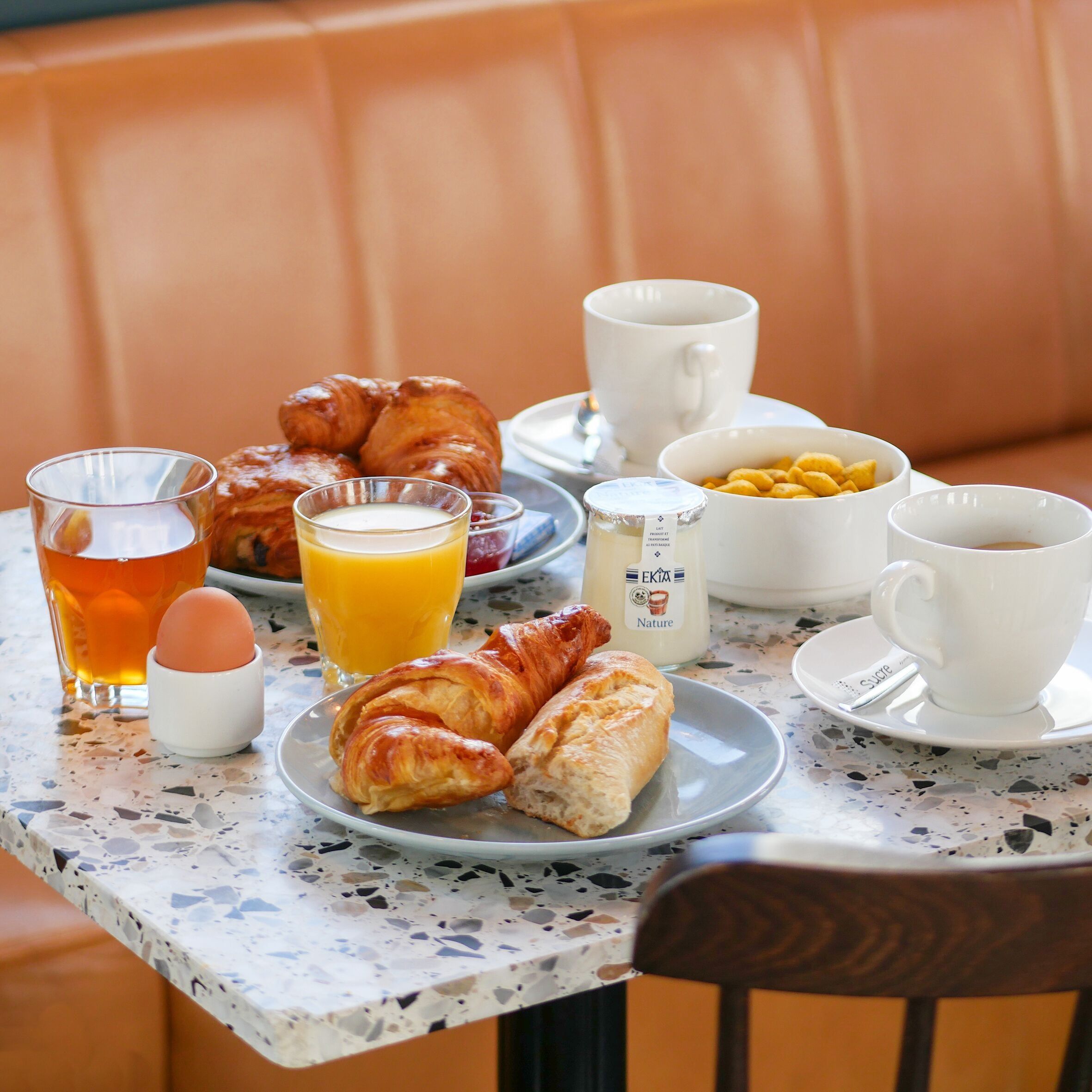 Disposição para o café da manhã com croissants, um copo de suco de laranja, uma xícara de café e uma garrafa de leite sobre uma mesa.