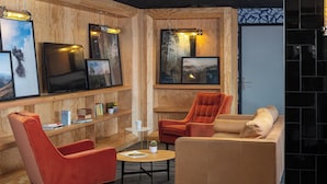 A cozy lounge area with wooden paneling, a large flat-screen TV, comfortable seating, and framed artwork on the walls. - Eklo Hotels Paris Roissy CDG Airport (Roissy-en-France)