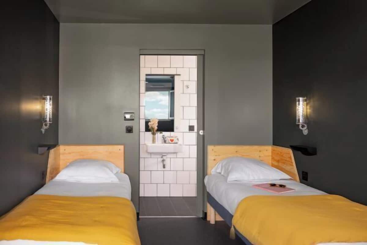 A room with two beds, a bathroom with a mirror, and a door.