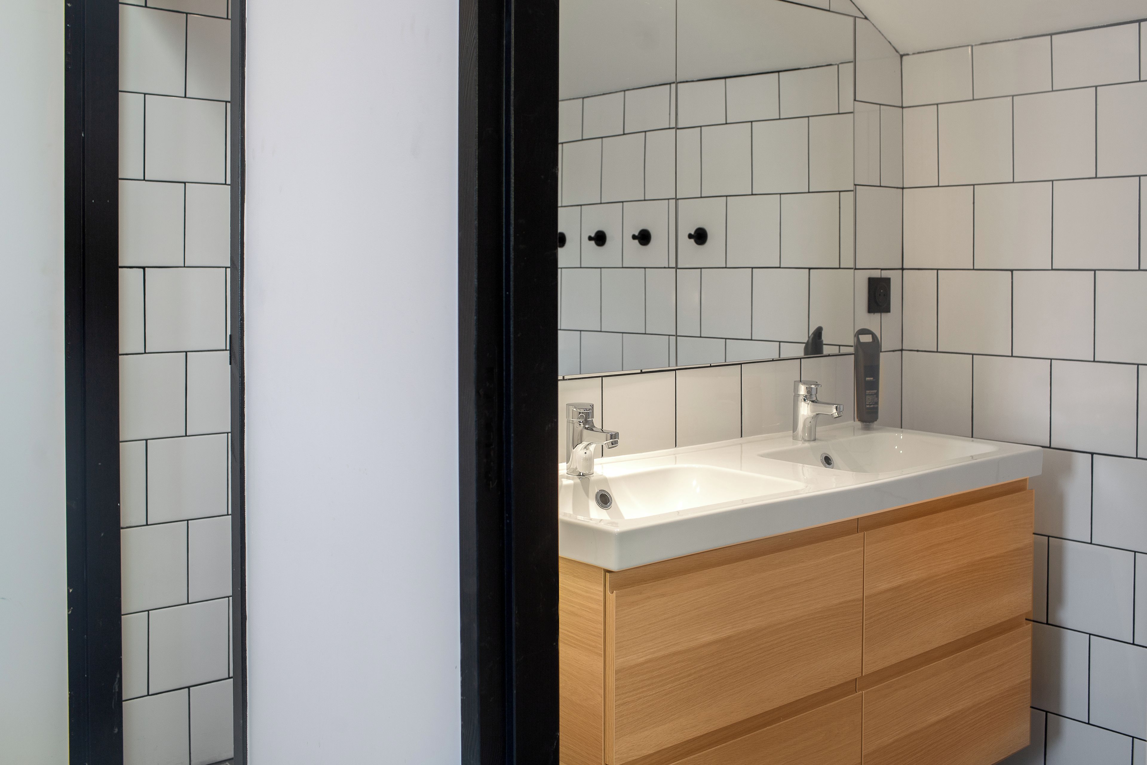 A modern bathroom with a white sink, wooden cabinets, and a tiled wall.