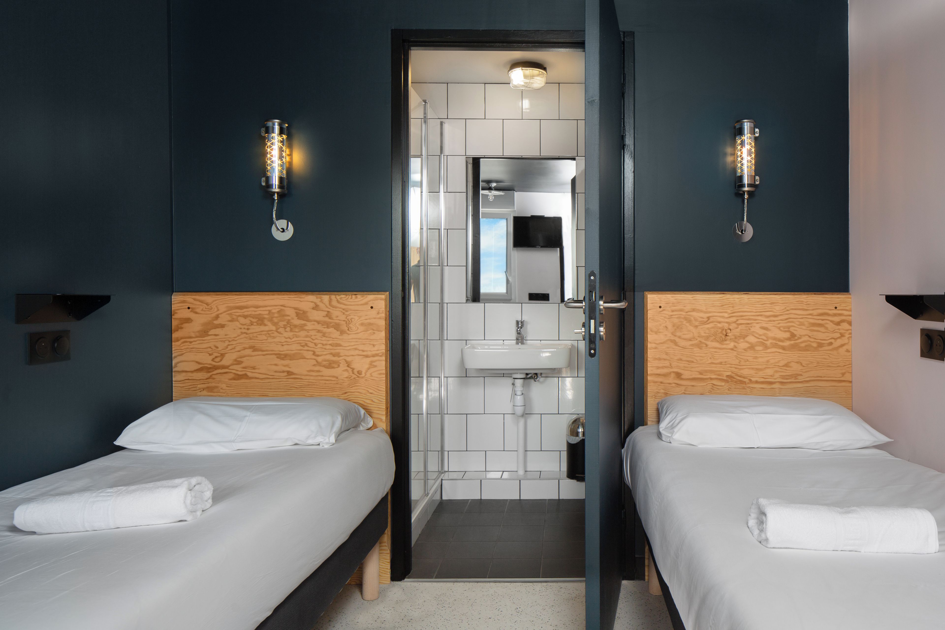 Ein Hotelzimmer mit zwei Betten, einem hölzernen Kopfteil, einem Waschbecken und einem Spiegel.