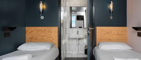 Ein Hotelzimmer mit zwei Betten, einem hölzernen Kopfteil, einem Waschbecken und einem Spiegel.