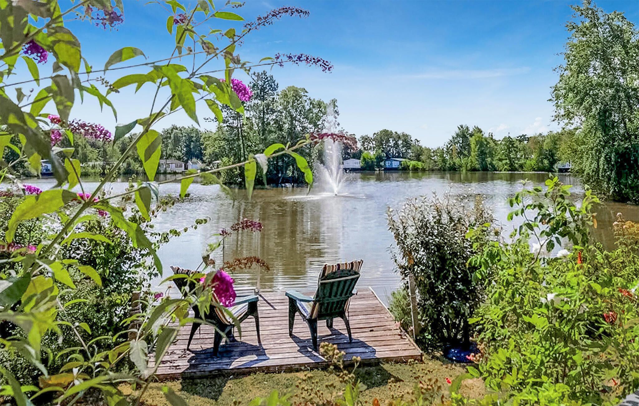 En rogivande plats vid en sjö med en träbrygga, två stolar och en fontän.