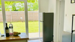 Eine moderne Küche mit Kühlschrank, einer Holzauslage und Blick auf einen grünen Garten durch Glastüren.