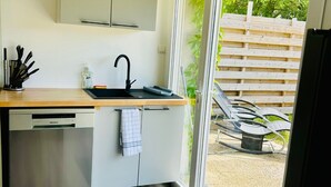 Eine moderne Küche mit integriertem Geschirrspüler, einem Spülbecken mit Wasserhahn und einem Fenster mit Blick auf eine Holzterrasse.