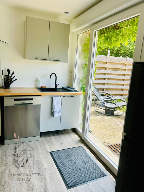 Cozinha moderna com máquina de lavar louça embutida, pia com torneira e janela com vista para um deck de madeira.